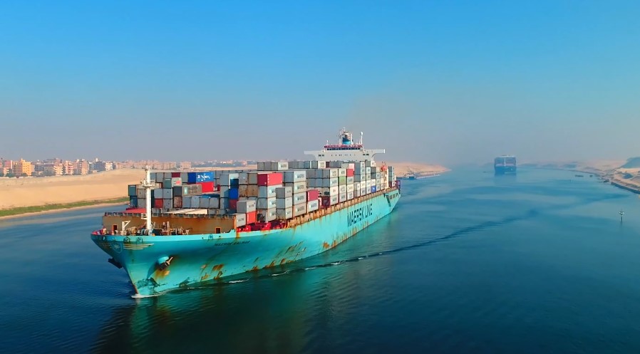 A colossal container ship, a vibrant turquoise, cuts through the azure waters of the Suez Canal