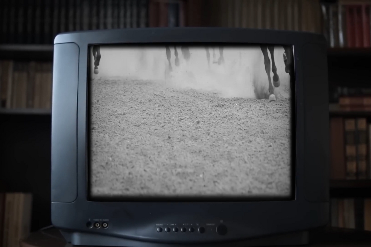 Black and white footage of horse hooves racing on dirt track shown on a vintage TV during Melbourne Cup coverage