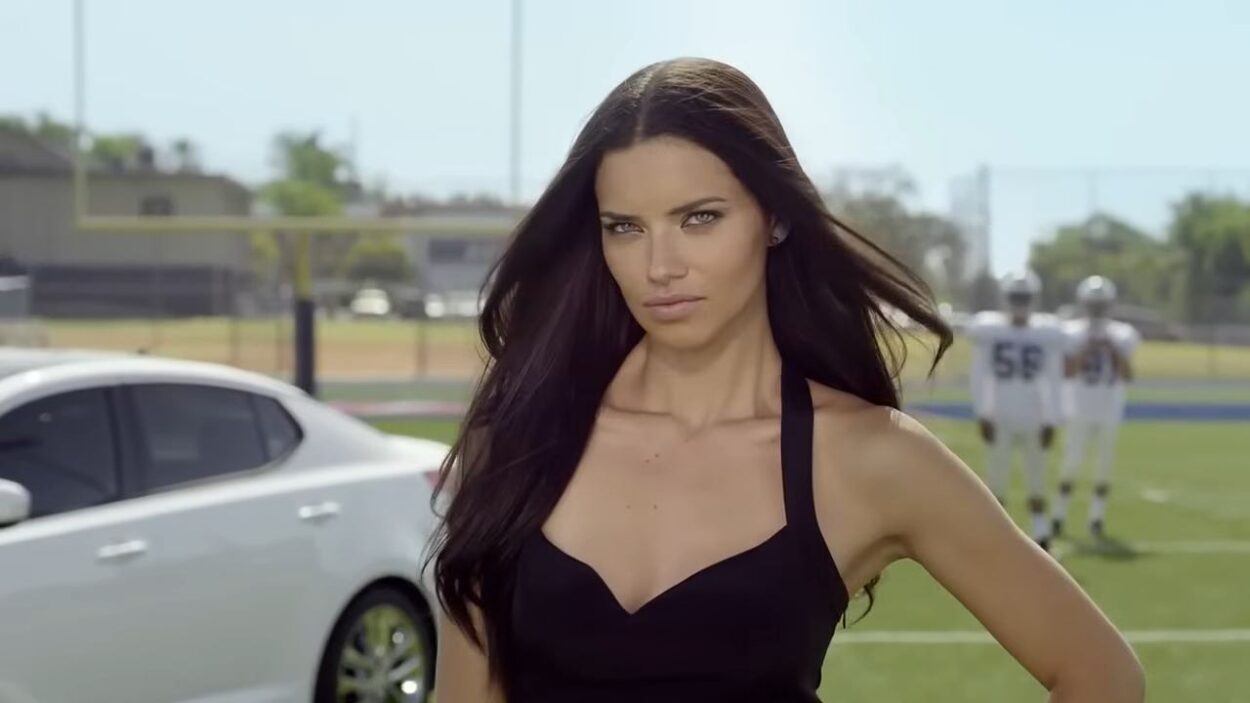 Woman in a black dress standing near a silver car and football players