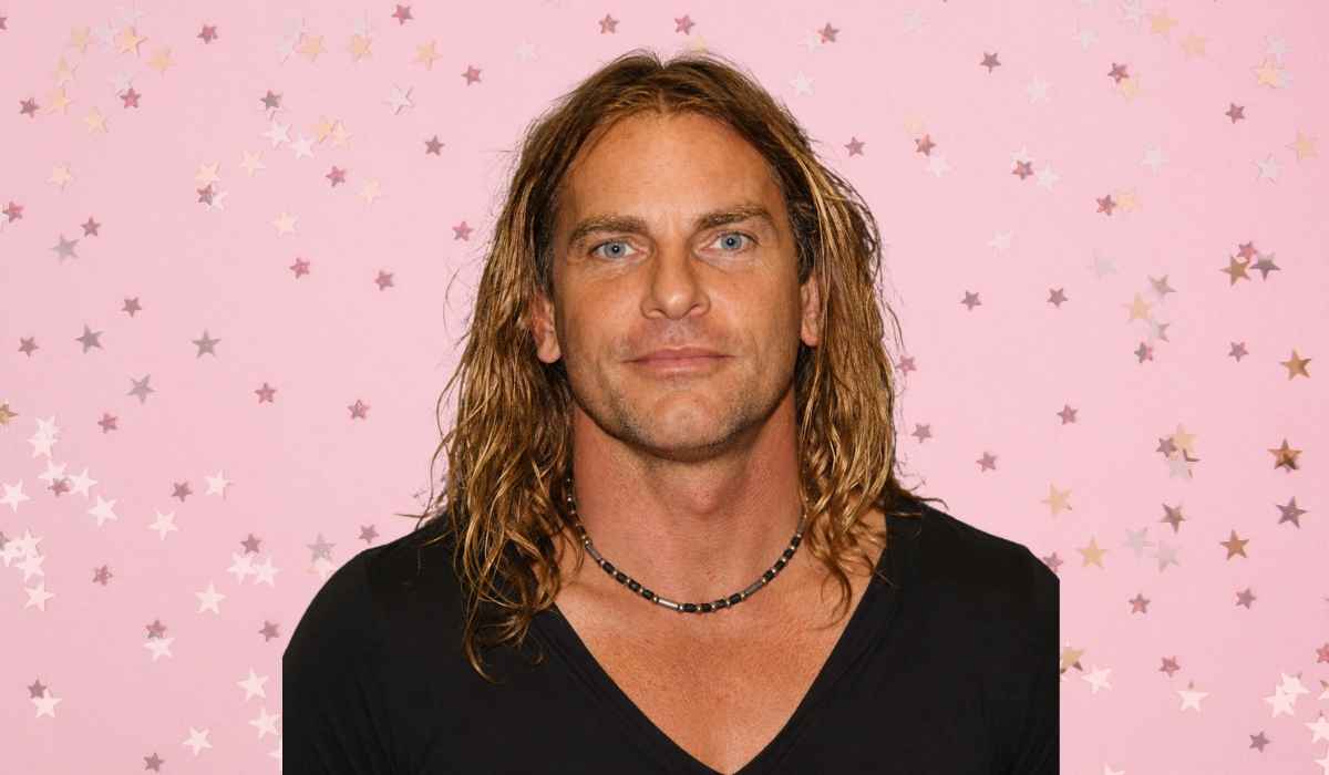 Evan Stone wearing a black V-neck shirt against a pink background with scattered stars