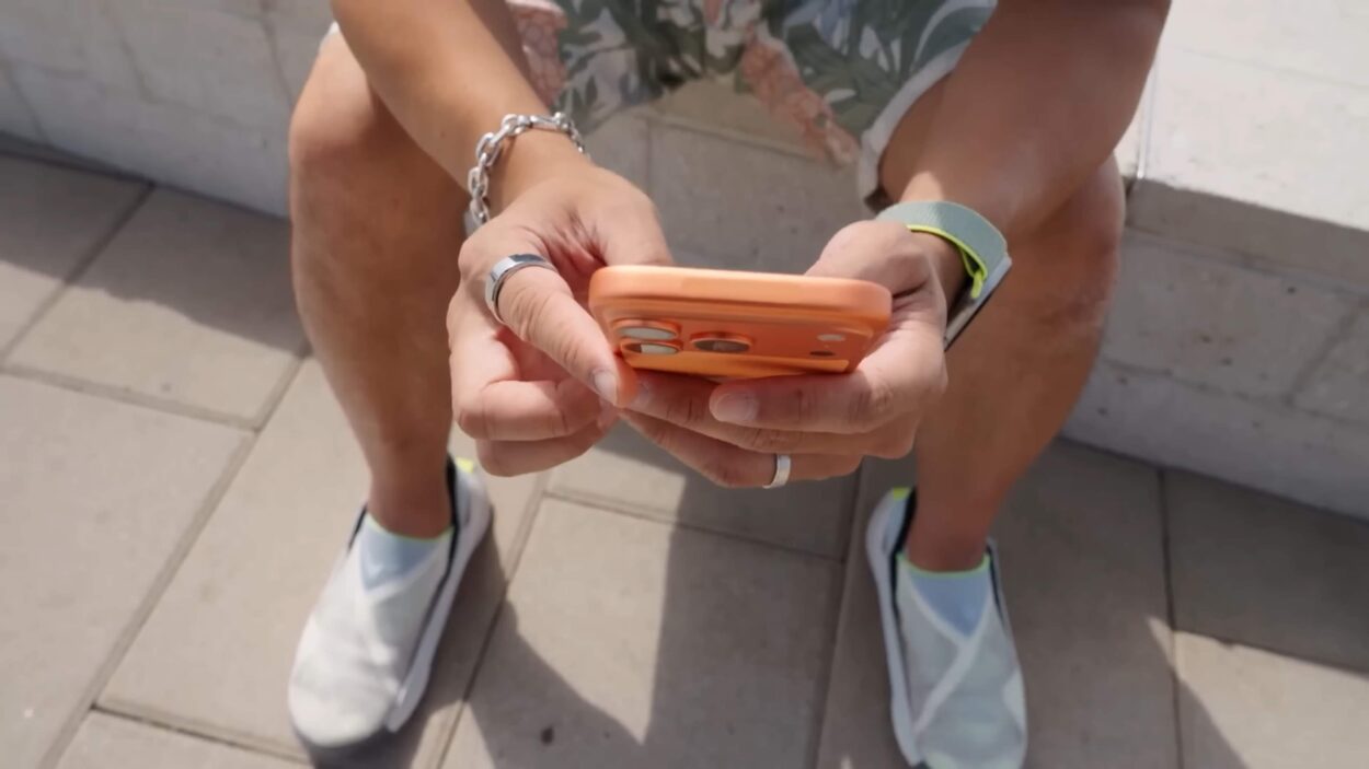 Person using an orange iPhone while sitting outside.