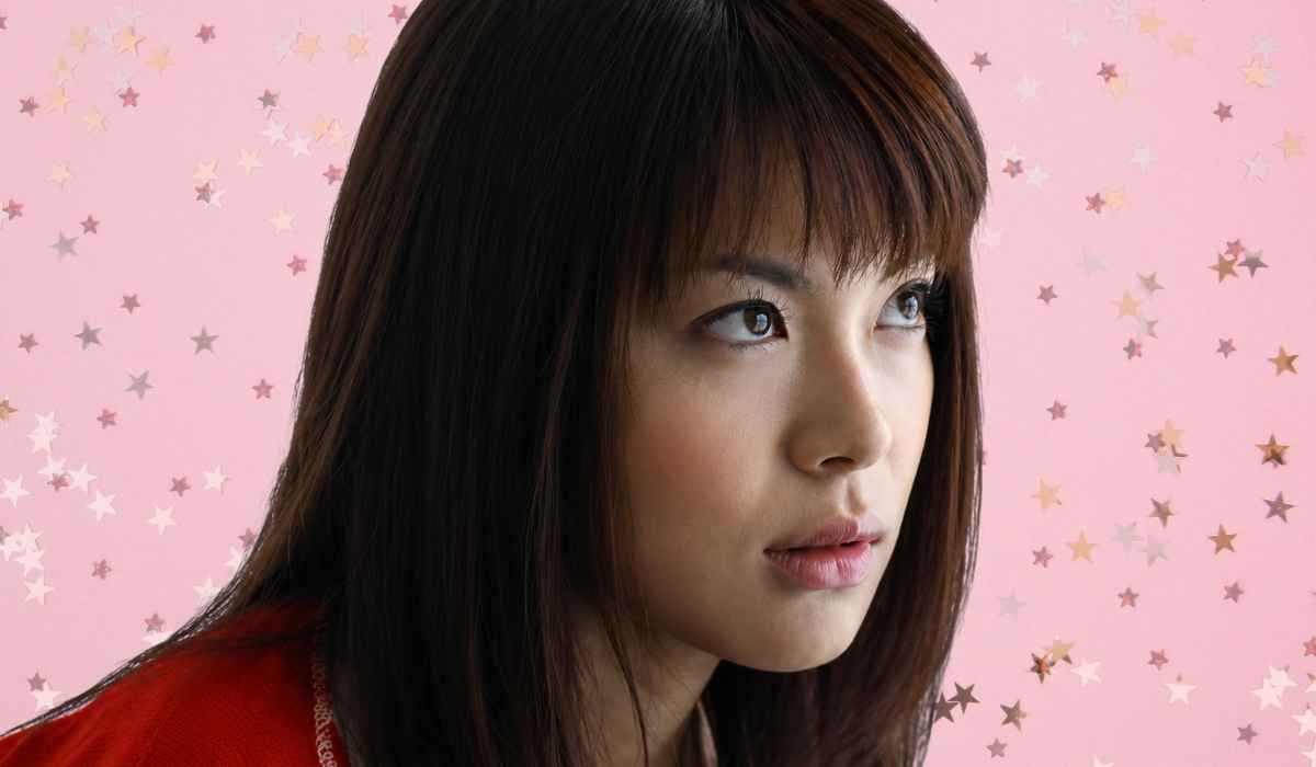 Close-up portrait of Maria Takagi looking to the side with a pink star-pattern background