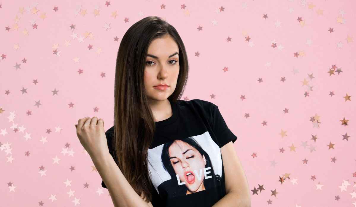 Sasha Grey wearing a black graphic T-shirt against a pink background