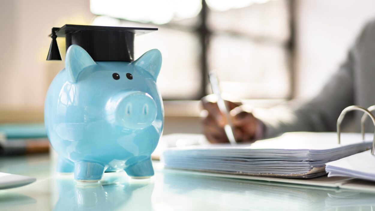 Piggy bank with a graduation cap beside student loan paperwork.