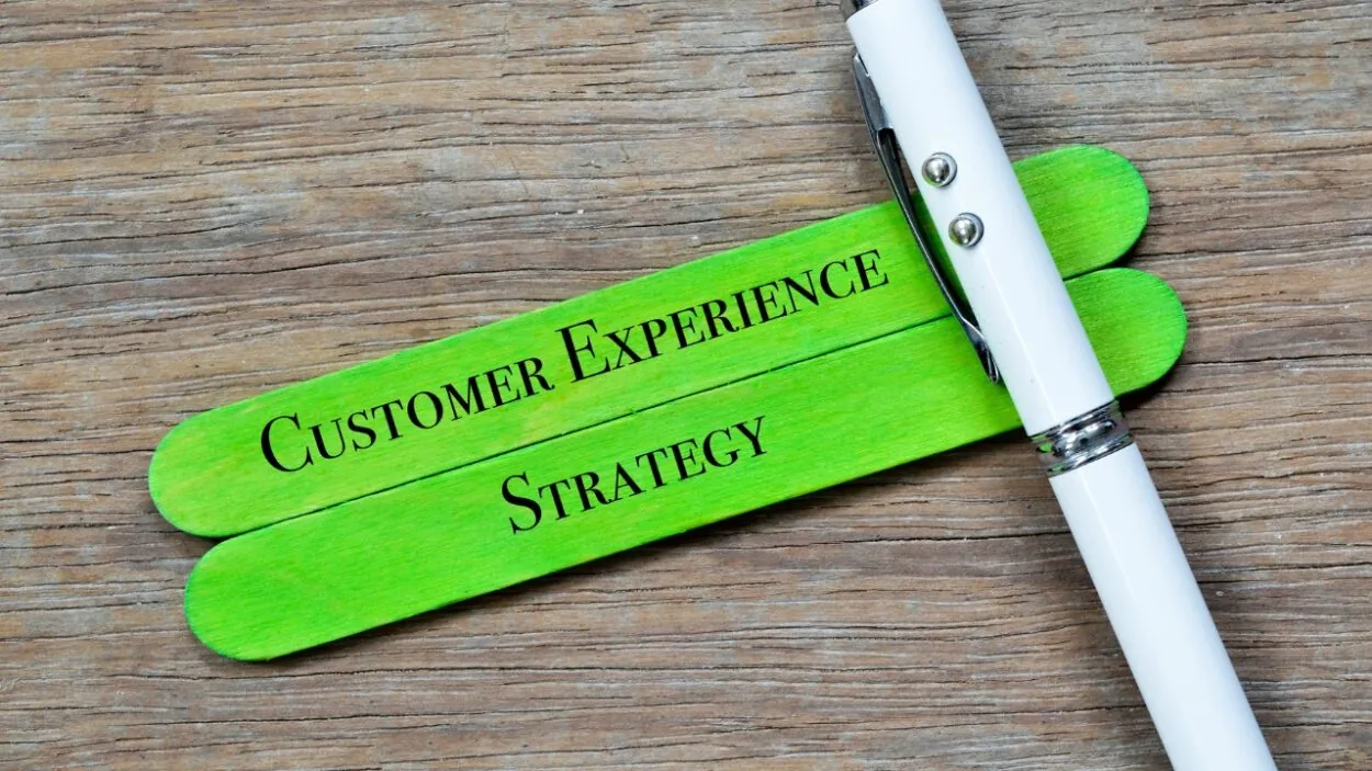 Green sticks display the words Customer Experience Strategy beside a white pen.