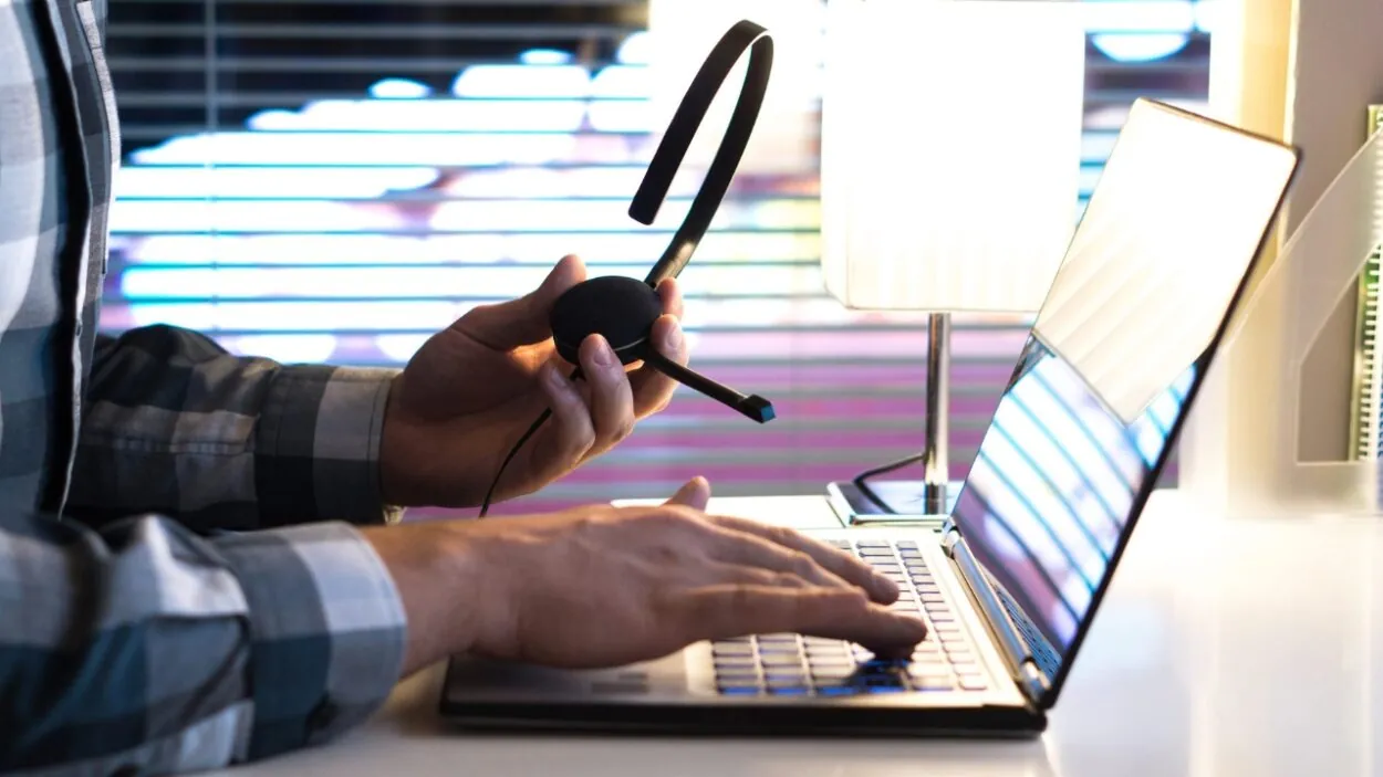 A support agent uses a laptop with a headset at a desk.