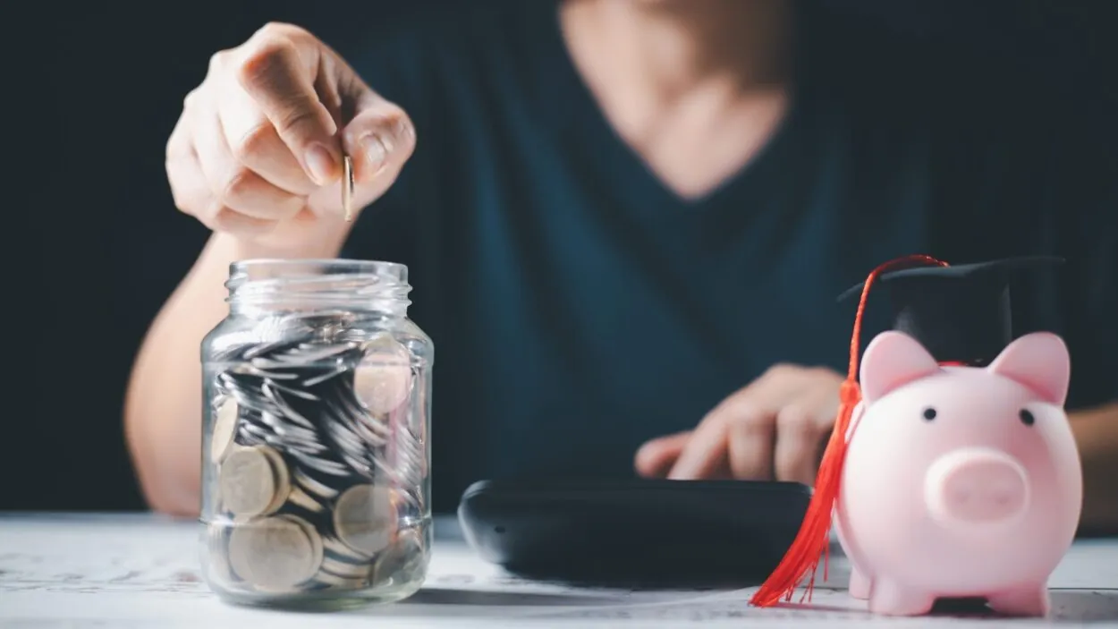 Student saves coins beside a piggy bank with a graduation cap