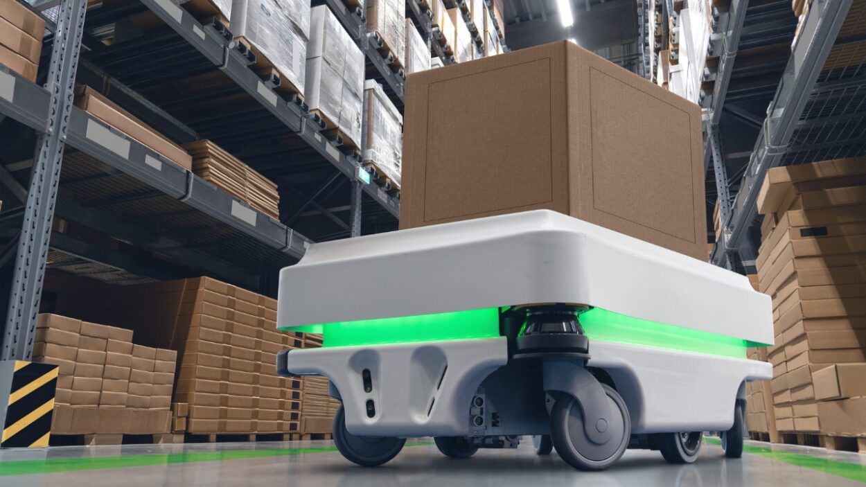 Autonomous warehouse robot carries a large cardboard box through storage aisles
