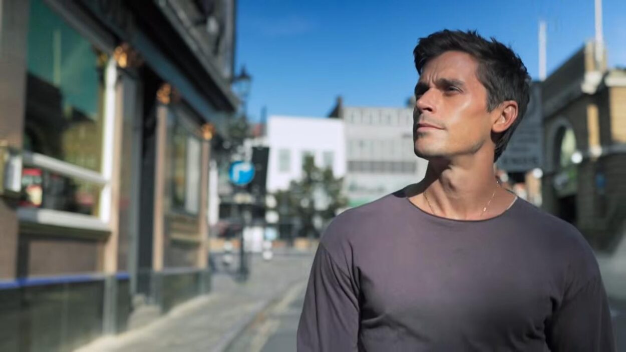 Antoni Porowski wearing a gray shirt while standing on a sunlit city street.