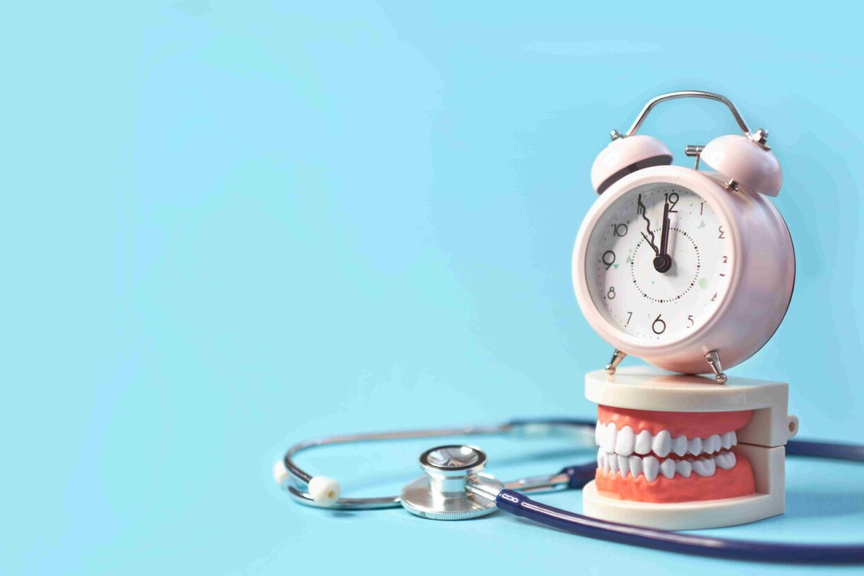Pink alarm clock on a dental model beside a stethoscope against a blue background.