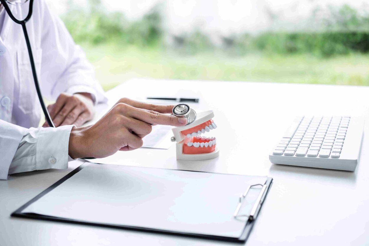 Doctor holding a stethoscope over a dental model during a medical consultation.