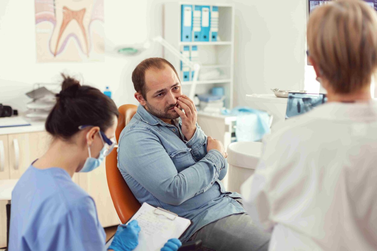 Patient experiencing tooth pain while discussing dental treatment with healthcare professionals.