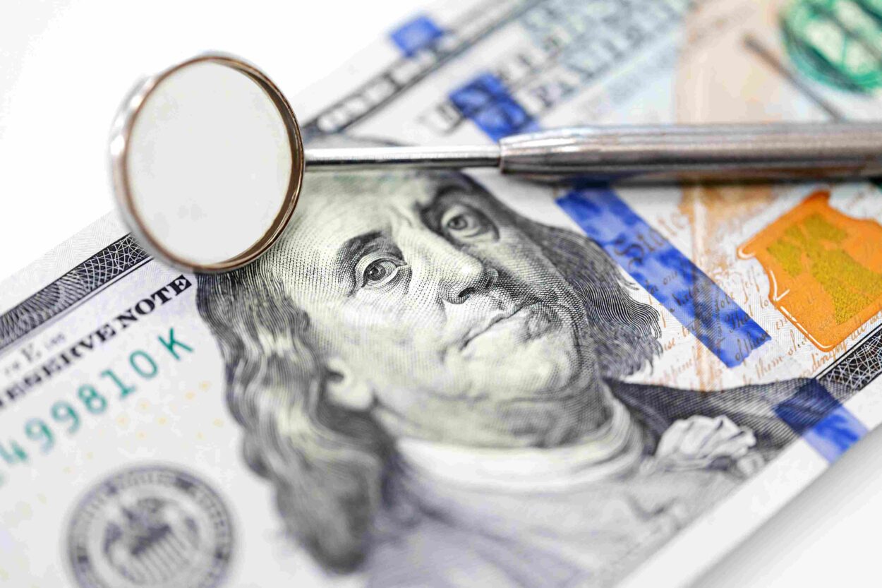 Dental mirror and probe resting on a $100 bill, illustrating dental treatment expenses.